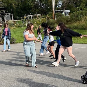 A large group of Rock Point School students laugh and play together in a school yard game running and holding hands together.