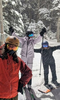 Three people from Rock Point School pose together on top of a snowy mountain in their skiing and snowboarding gear before starting their active run down the mountain. 