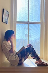 A Rock Point School student sits in a window well at the school reading during the winter months in Vermont, practicing the Scandinavian concept of hygge.